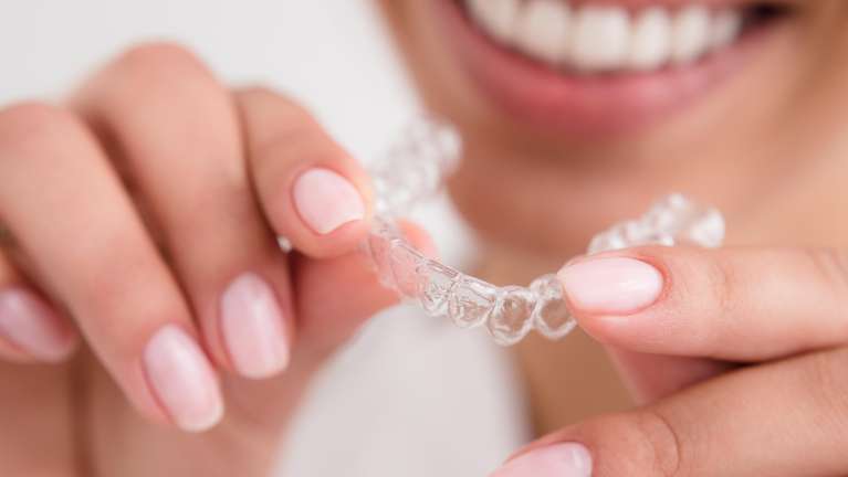 patient holding clear plastic aligner | invisalign farmington hills mi